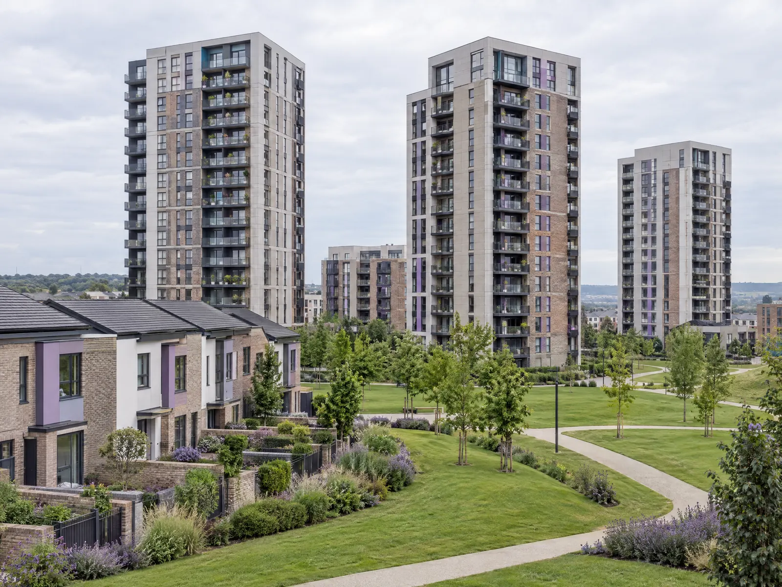 Tall residential towers above townhouses, lawns and curving walking paths under a cloudy sky