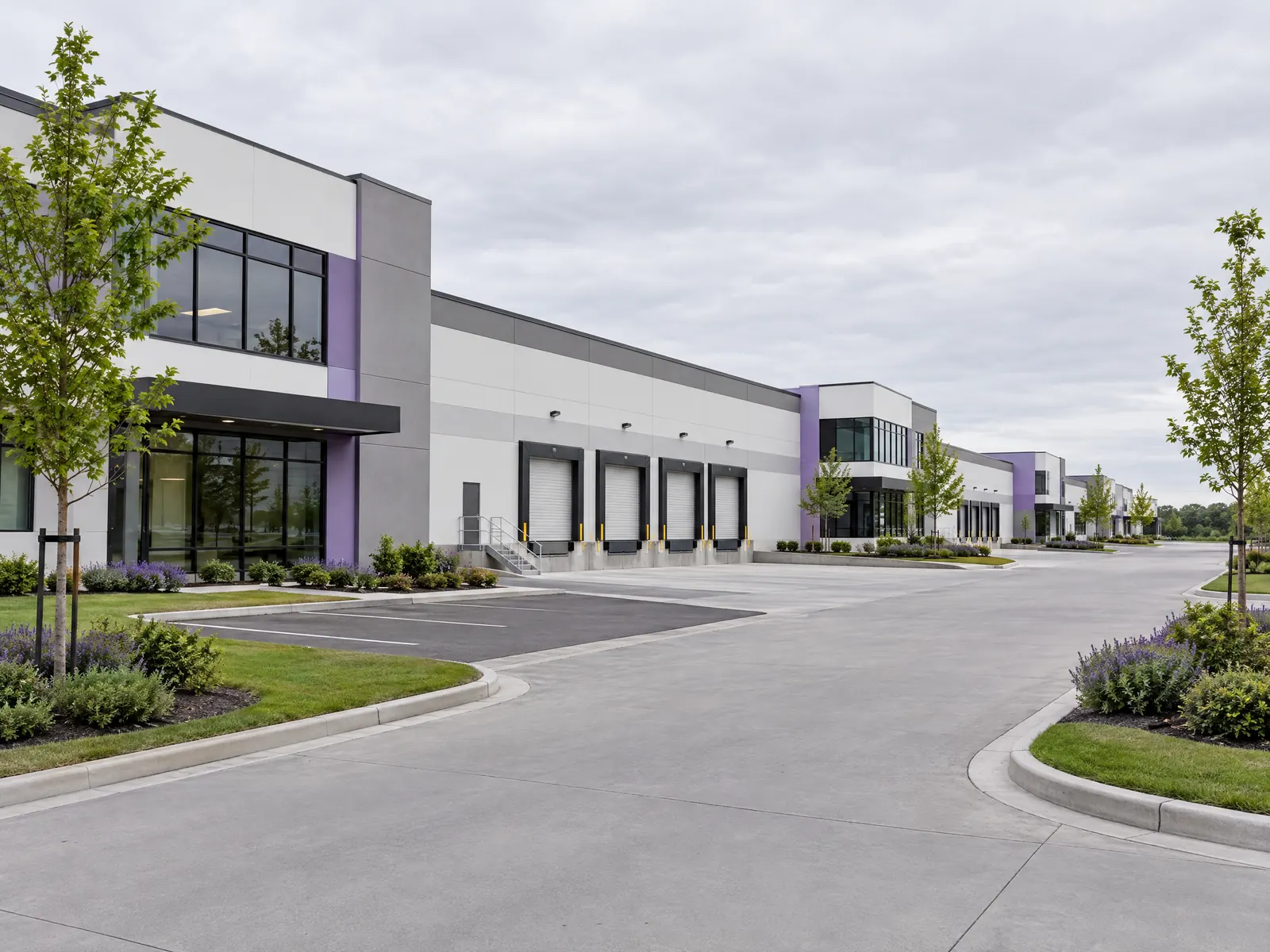 Modern warehouse buildings with loading docks and landscaped lawns under an overcast sky
