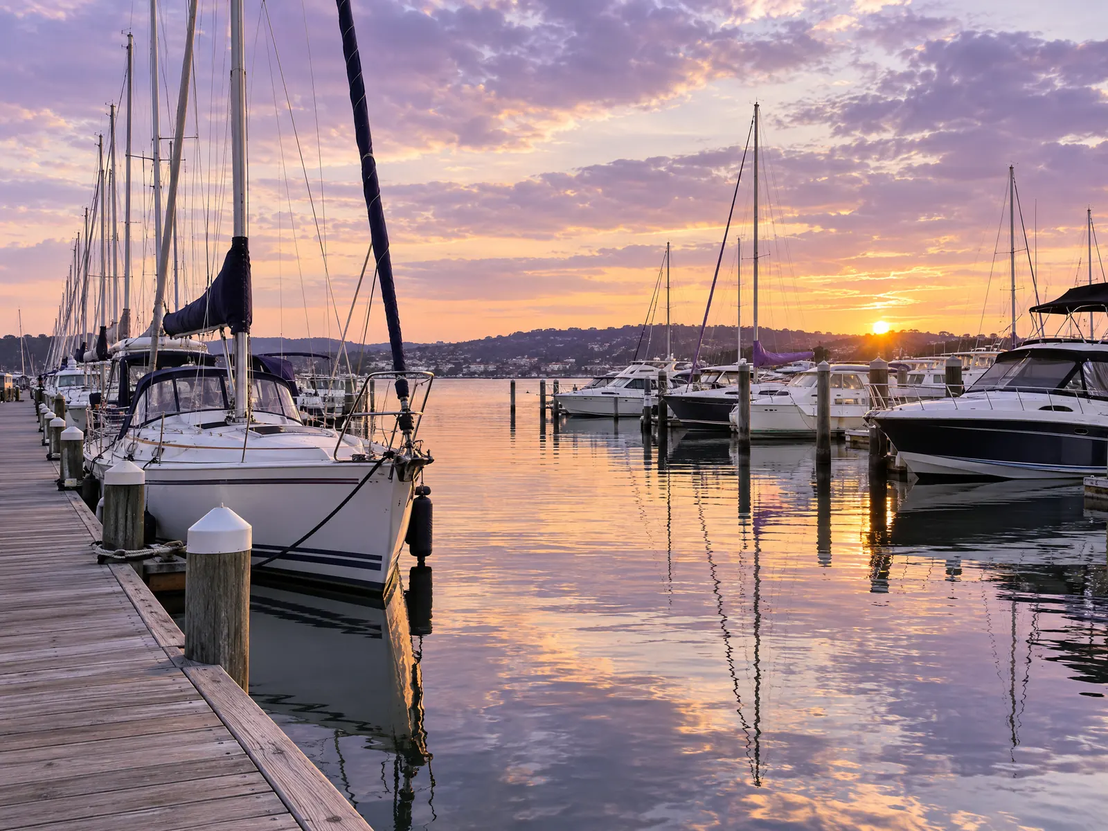 Marina with sailboats and motorboats at wooden docks under a lavender sunset sky