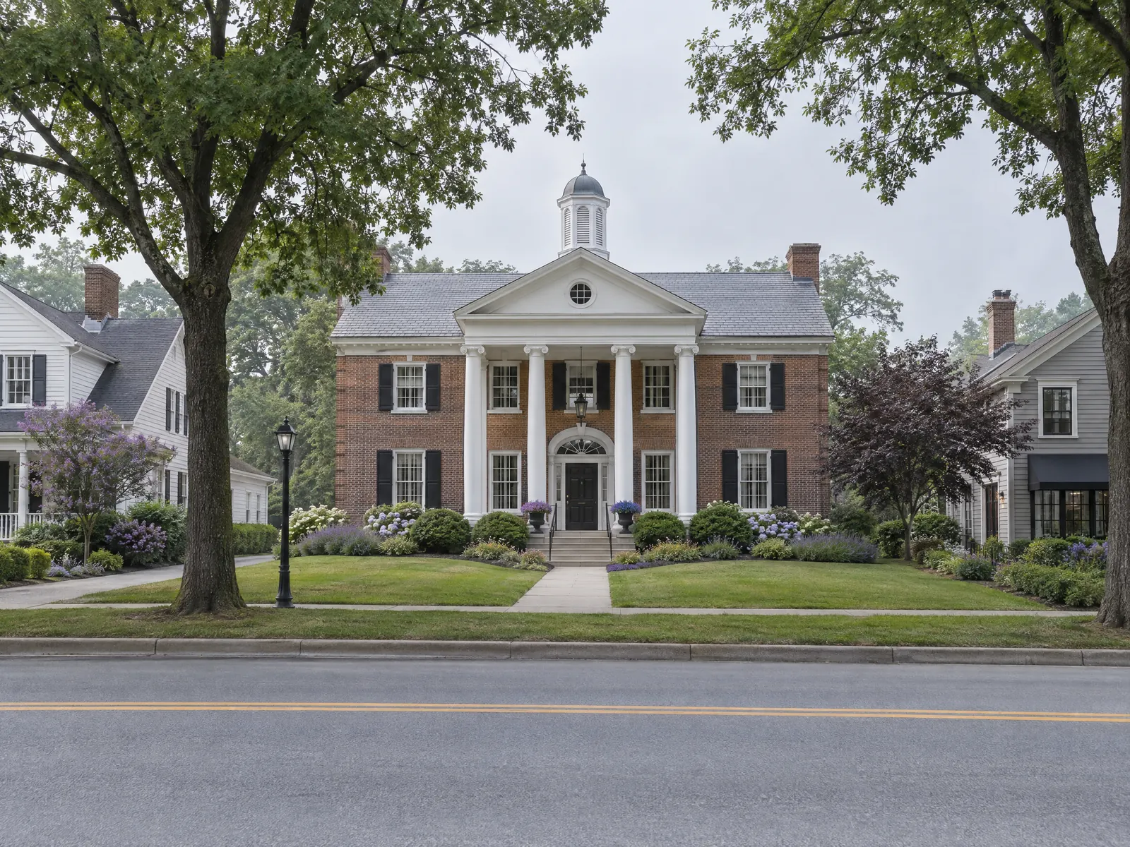 Brick colonial building with a white columned portico and cupola on a shaded lawn